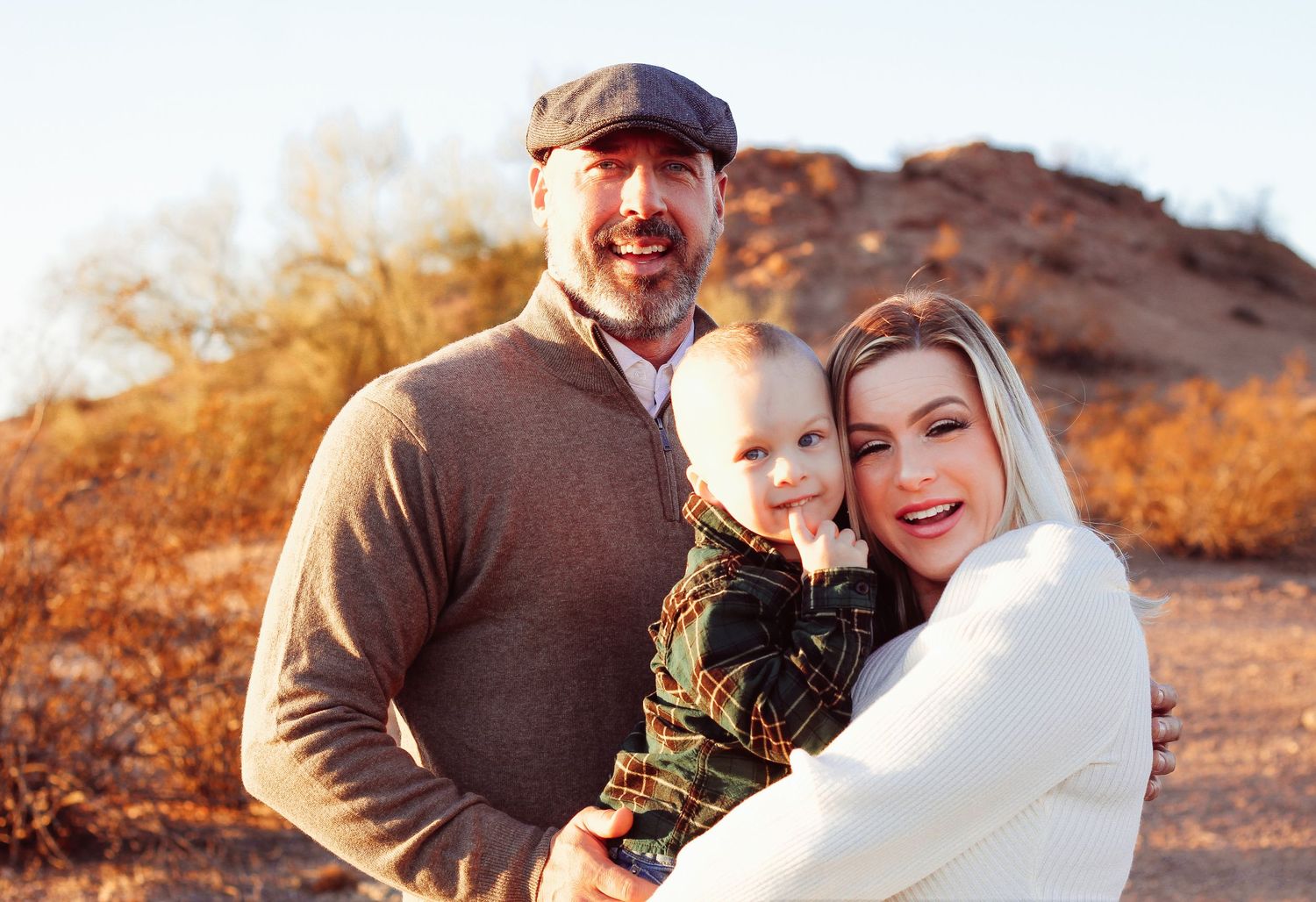 Family portrait in desert setting during golden hour with warm tones and mountain backdrop.