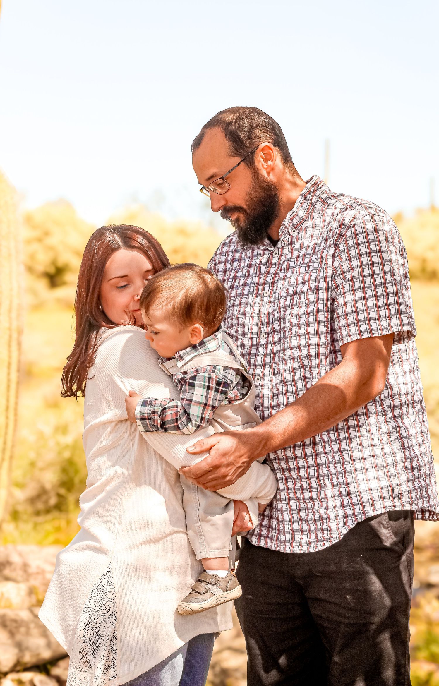 Family shares tender moment outdoors in warm sunlight against natural landscape.