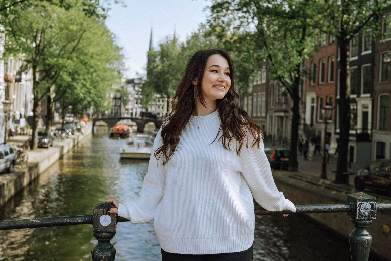 Smiling woman on canal bridge with scenic Amsterdam background.