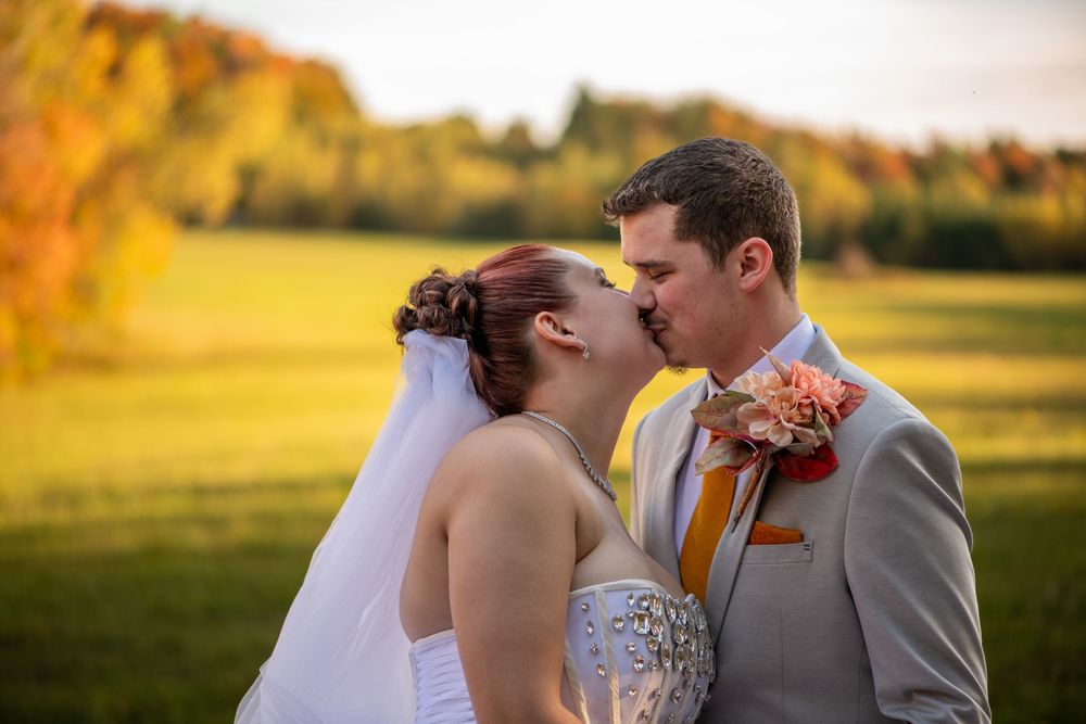 A couple shares a romantic kiss in a golden sunlit field during their autumn wedding celebration.
