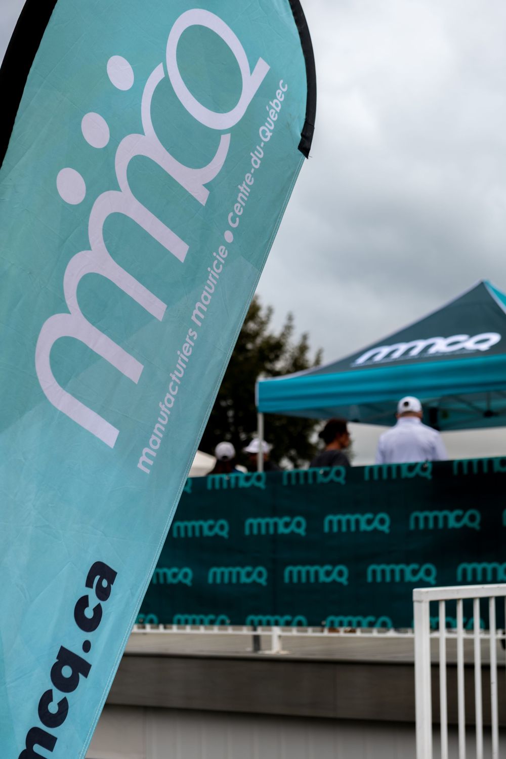 MMCQ Manufacturiers Mauricie Centre-du-Quebec branded teal banner flag and tent at outdoor event.