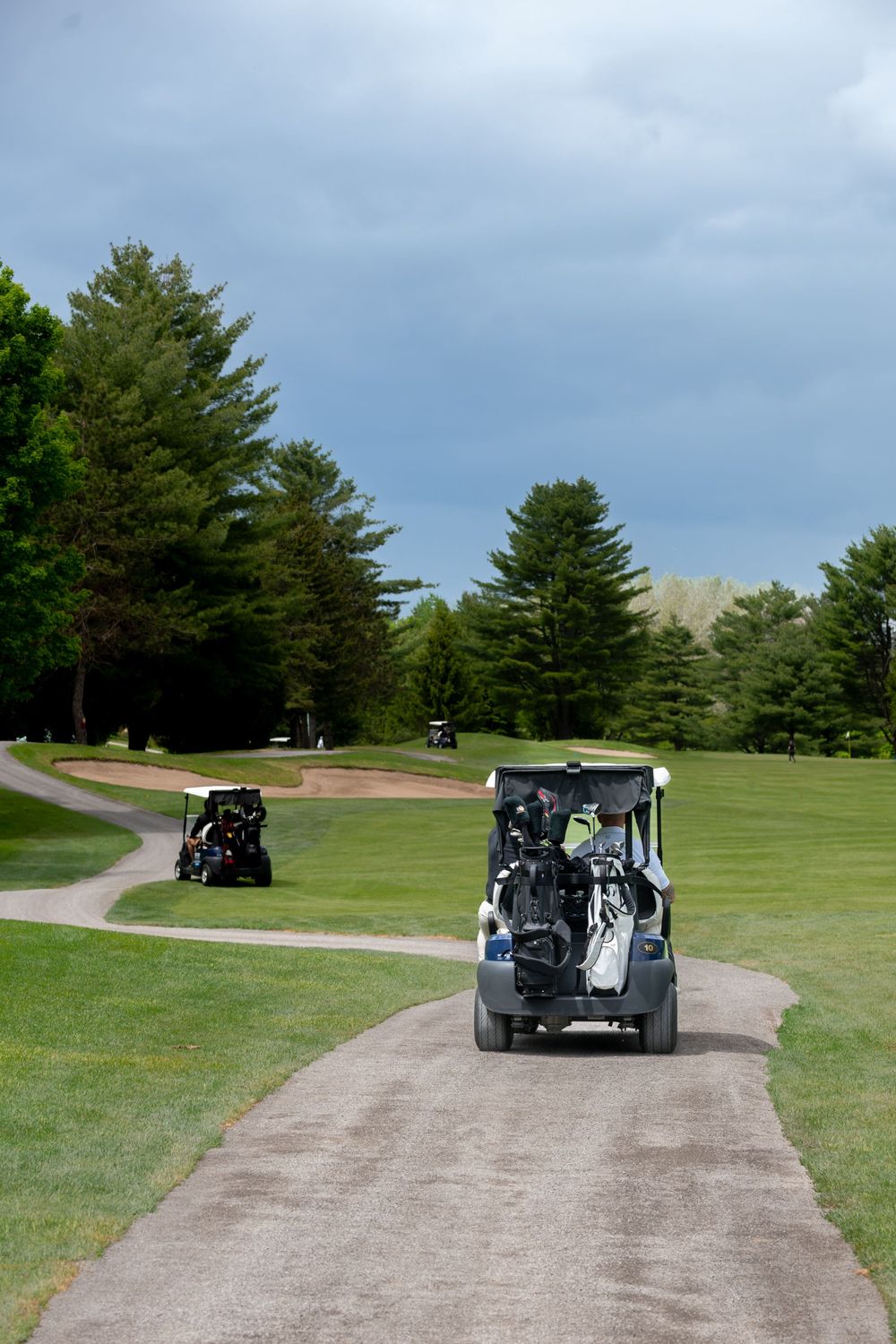 Two golf carts traveling along a winding path on a lush green golf course under a cloudy sky.