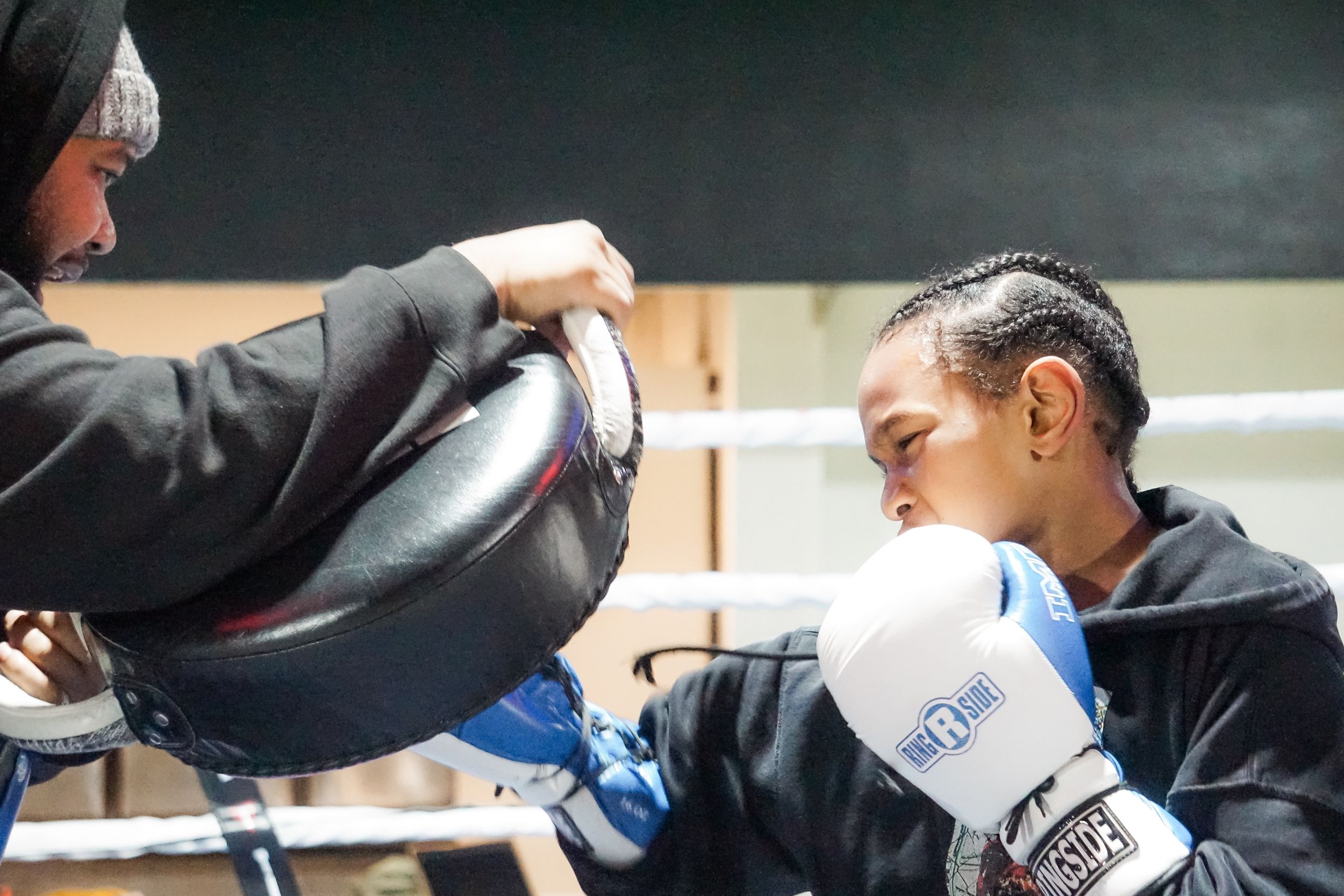 Two boxers during training session, one holding pads while other prepares to strike wearing white gloves.