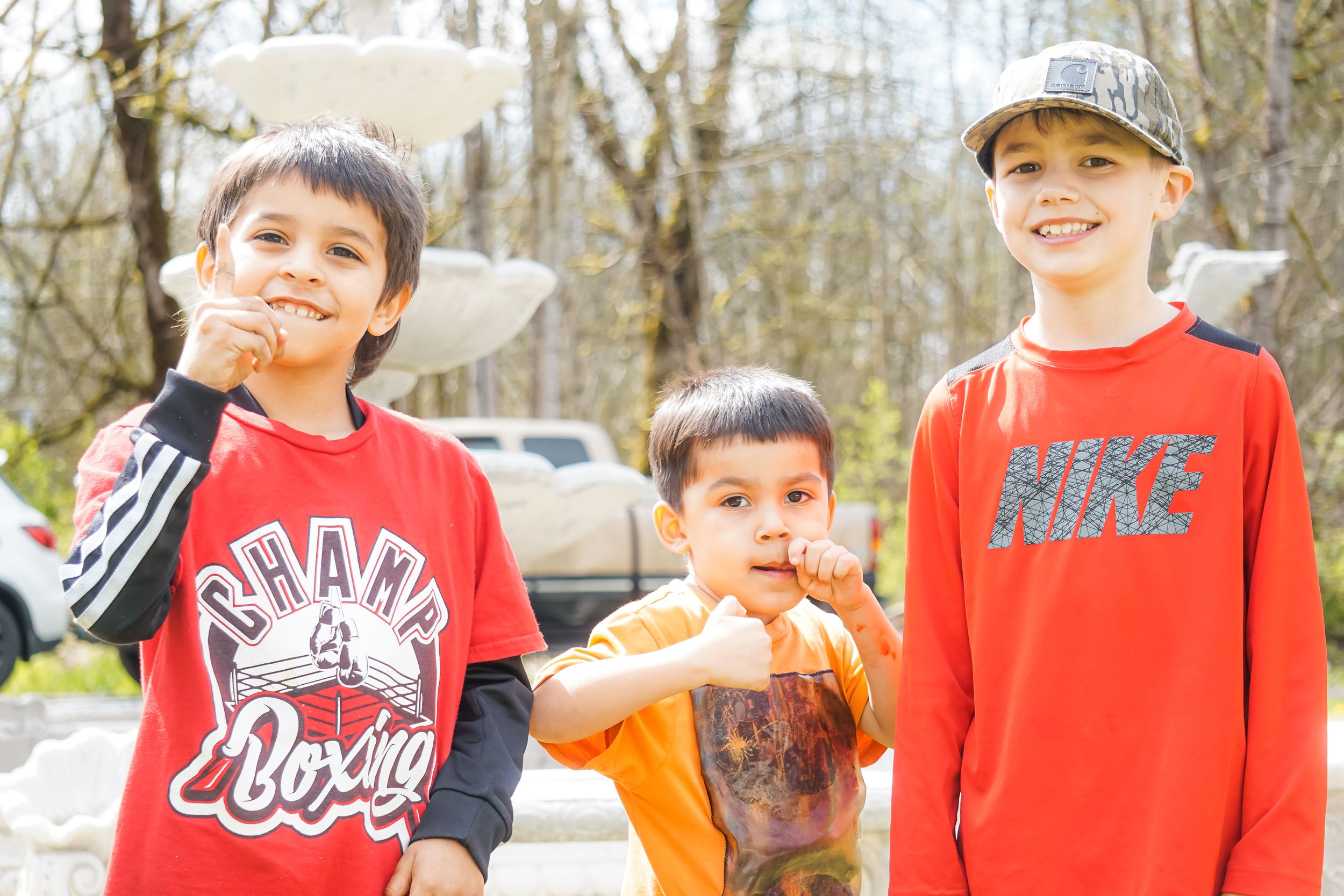 Three children in bright red shirts stand together outdoors on a spring day among bare trees.