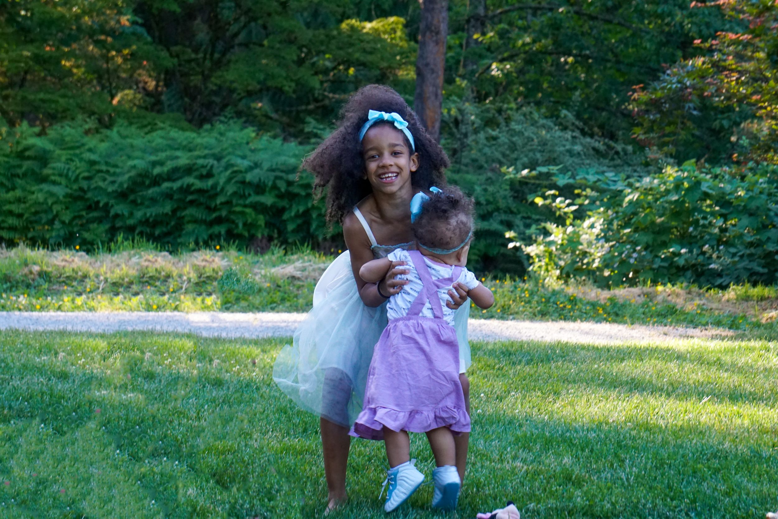 Two children in summer dresses play together on a sunny green lawn.
