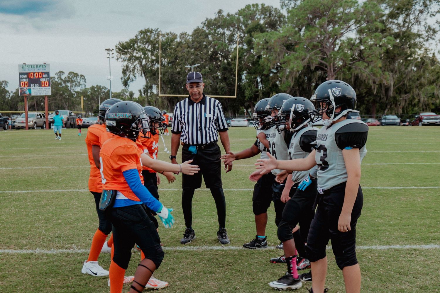 A referee conducts a coin toss between two youth football teams on a green field.