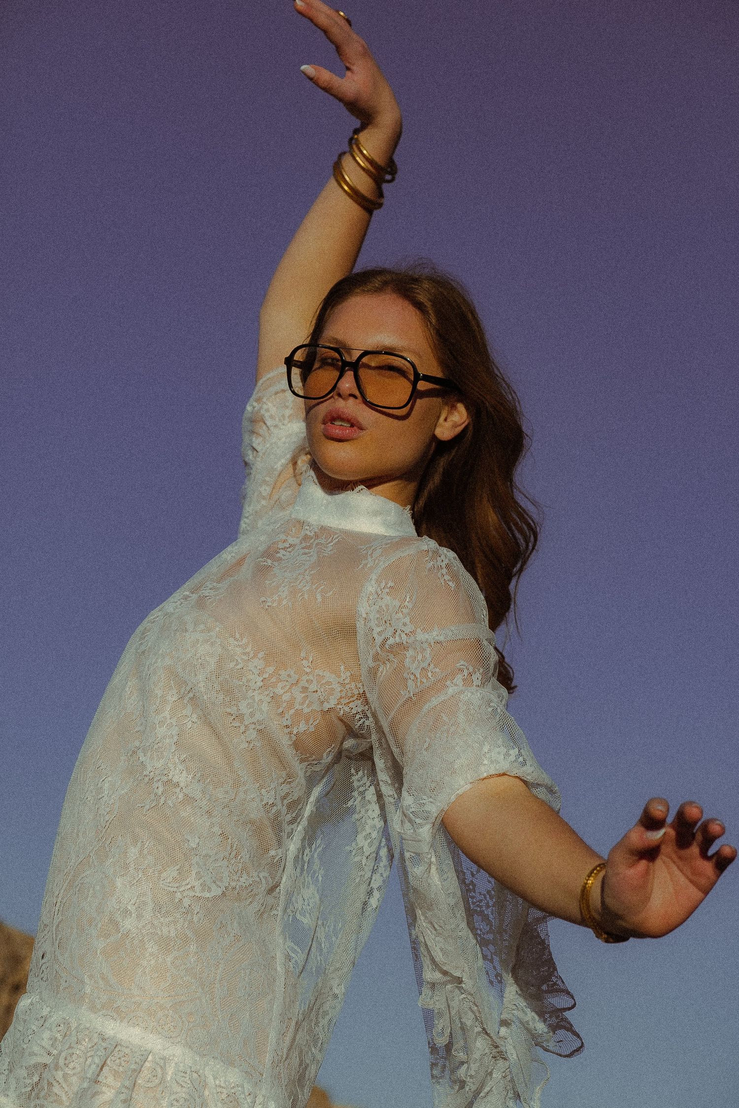 Artistic fashion photo with model in sheer white lace blouse against dusky background.