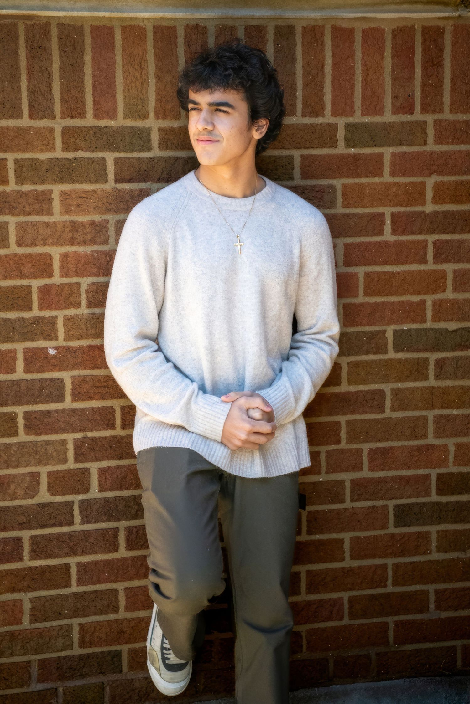 A casual portrait against a brick wall featuring someone in a light gray sweater.