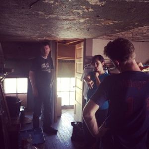 Film crew working in a dimly lit indoor location with camera equipment.