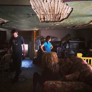 People filming in a room with damaged ceiling and vintage furniture.