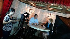 Film crew setting up camera equipment in a restaurant with brick walls and red curtains.