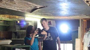 Film production crew working with lighting and camera equipment in a basement setting.