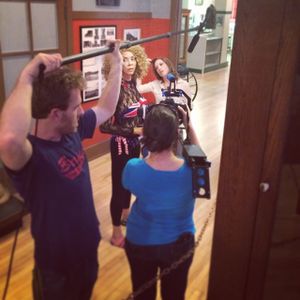 Film crew members adjusting boom microphone and camera equipment during indoor shoot.