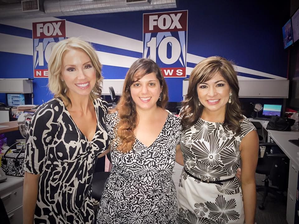Three women pose together at a FOX 10 news station set wearing patterned dresses.