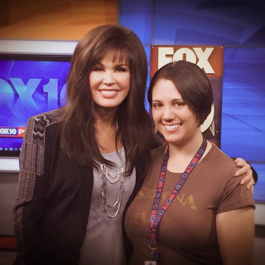 Two people pose together in front of a FOX10 news station backdrop.