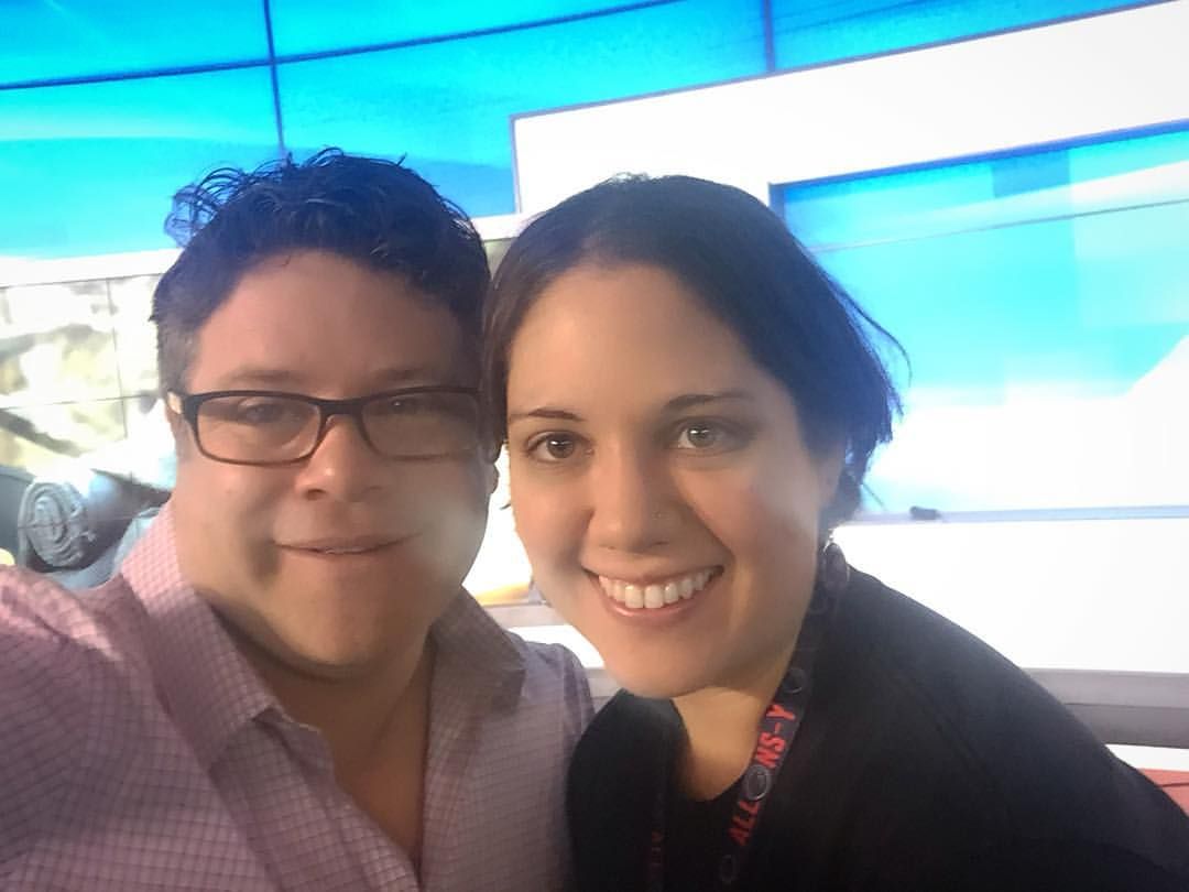 Two people take a selfie together with a blue backdrop behind them.