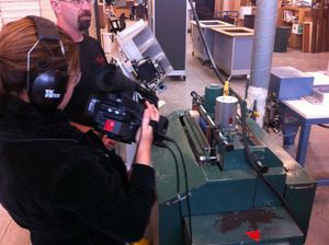 Camera operator filming close-up of technical equipment on a green workbench.