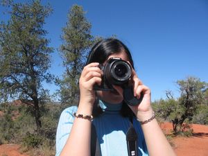 Person taking photos with a DSLR camera against a blue sky and pine trees.