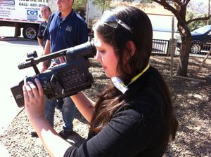 Camera operator films outdoor footage with a professional video camera at a sunny location.