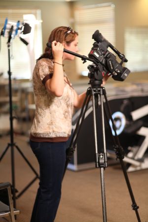 A videographer adjusts settings on a professional camera mounted on a tripod.
