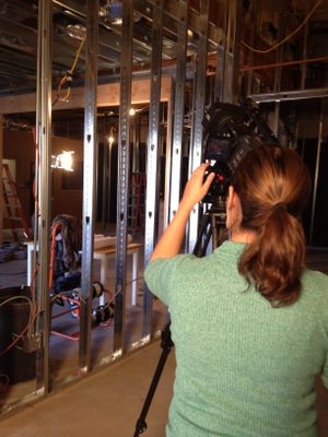 A camera operator films inside an unfinished construction space with exposed metal framing.