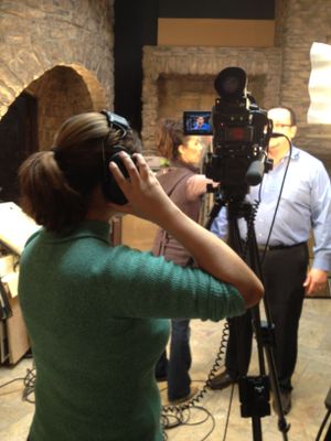 A videographer operates a professional camera in a stone-walled interior setting.
