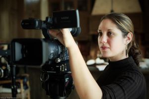 Camera operator filming with professional video equipment in an indoor setting.