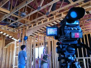 Professional video camera setup filming inside construction site with exposed wooden framing.