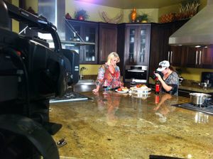 Film crew recording cooking scene on granite kitchen counter with professional lighting.