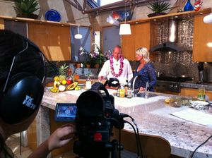 Video production crew filming a cooking segment in a rustic kitchen setting.