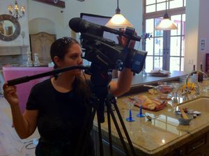 Camera operator adjusts professional video equipment in a bright indoor setting.