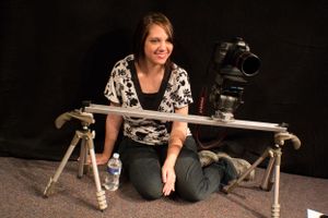 Videographer with camera equipment positioned on a slider against black backdrop.