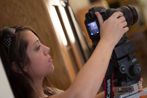 Photographer adjusts settings on DSLR camera while shooting indoors.