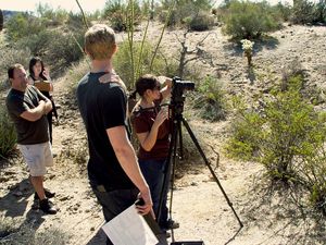 Group of photographers with cameras and tripods shooting in desert landscape.