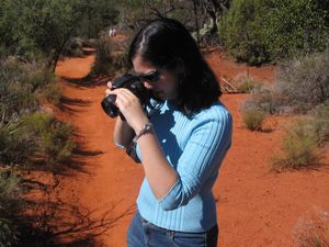 Photographer takes pictures on red dirt trail surrounded by desert brush.