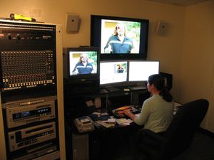 Video editor works in darkened control room with multiple monitors and mixing equipment.