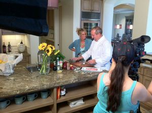 Camera crew films cooking segment in modern kitchen with sunflowers on counter.