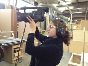 Video producer adjusts camera settings while wearing headphones in industrial space.