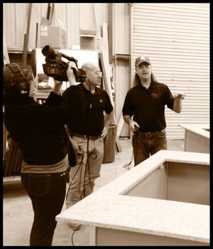 Three people discussing while looking at a counter surface during what appears to be a video production setup.