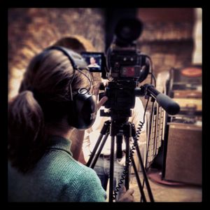 Camera operator using professional video equipment with headphones in a dimly lit setting.