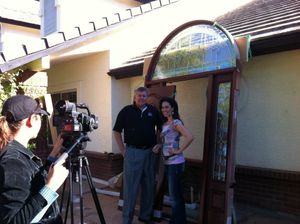 Outdoor filming session with camera crew and talent in front of a building entrance.