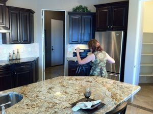 Videographer capturing footage in a modern kitchen with dark cabinets and granite countertops.