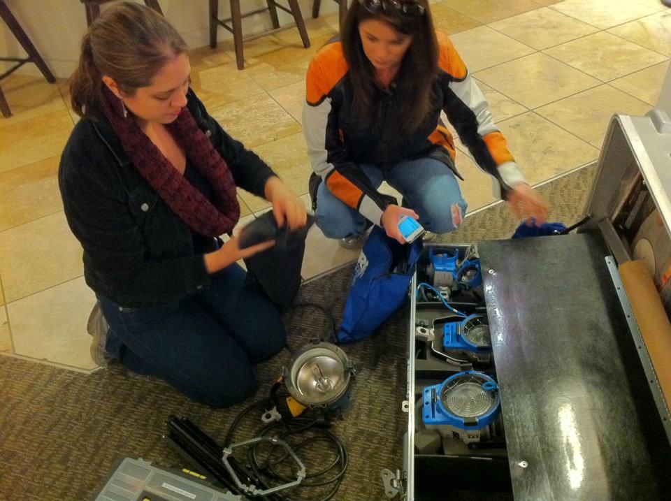 Two crew members examining technical equipment and lighting gear on the floor.