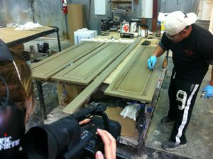 Behind-the-scenes shot of camera crew filming woodworking or furniture refinishing process.