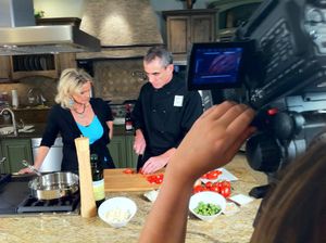 Kitchen filming session with crew capturing food preparation on granite countertop.