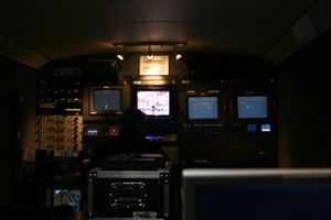 Dark control room with multiple TV monitors and production equipment.