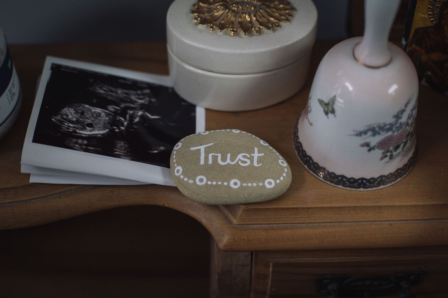 Still life arrangement with a decorative bell, black and white photograph, and a round plaque with 'Trust' written on it.