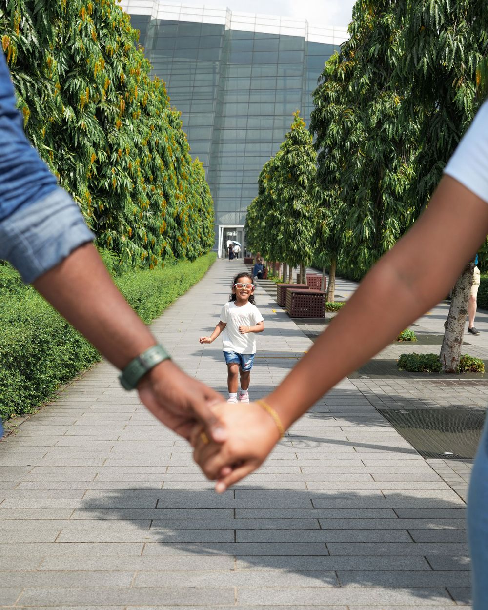 A child runs down a path between green walls while adults hold hands in the foreground.