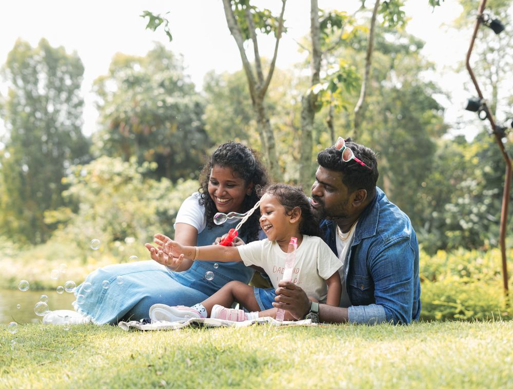A family relaxes together on grass in a sunny outdoor park setting.