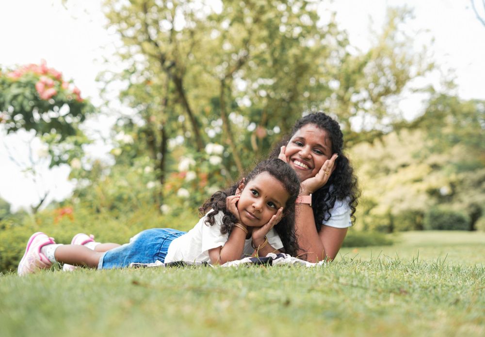 Two siblings relax together on green grass during a sunny day outdoors.
